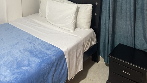 Une chambre à coucher comprenant un lit, une table de chevet, une commode et une fenêtre avec des rideaux.