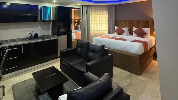 Une chambre d’hôtel moderne équipée d’une kitchenette, d’un canapé, d’un lit avec des oreillers et d’une salle de bain.