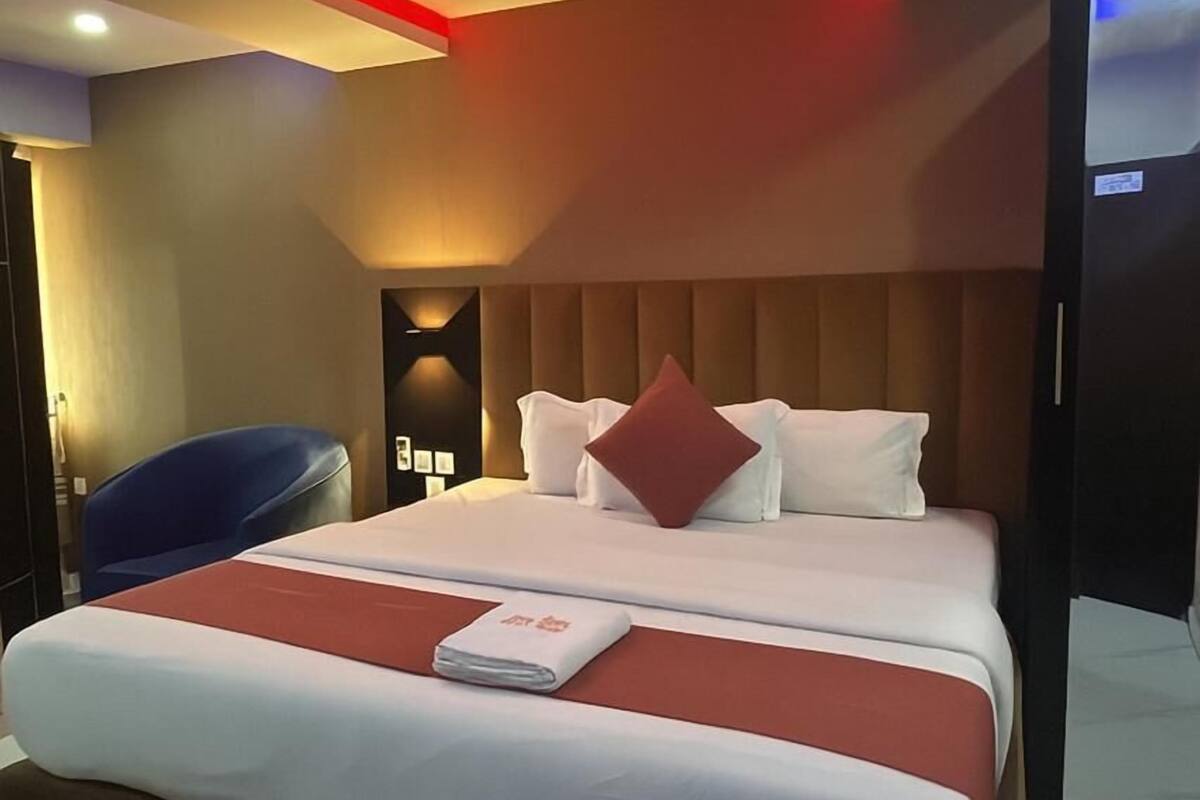A modern hotel room with a large bed, a blue chair, and a wall-mounted TV.