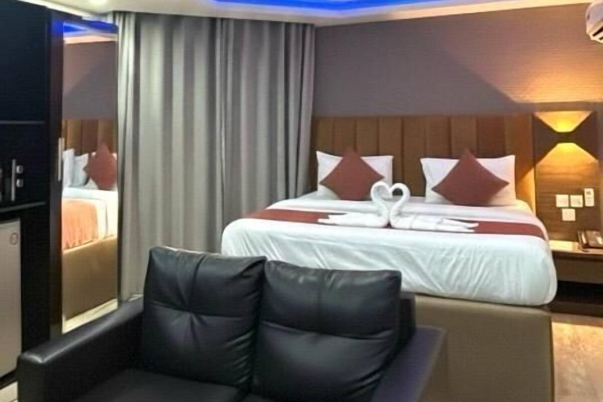 A modern hotel room with a bed, a black leather sofa, and a desk with a computer.