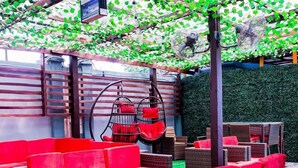 Un espace extérieur aménagé avec des canapés rouges et des fauteuils en osier, un mur végétal et des ventilateurs suspendus.