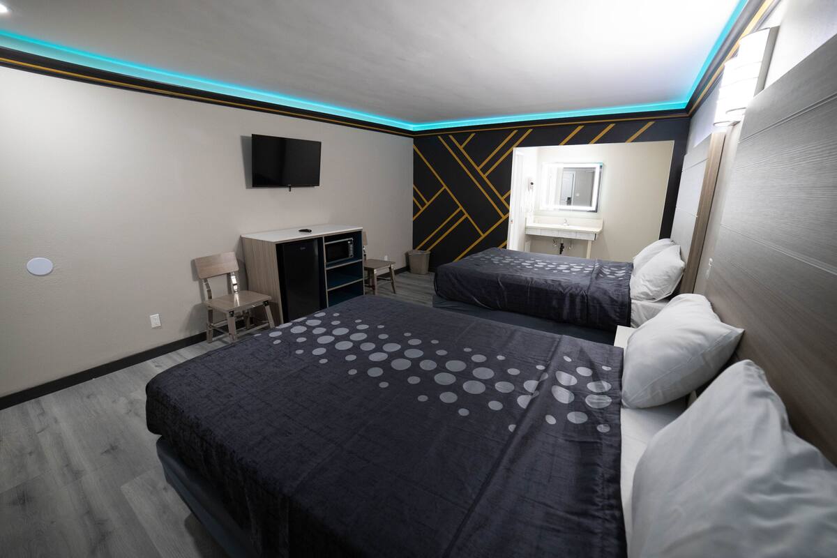 A modern hotel room with two beds, a desk, a TV, and a bathroom.