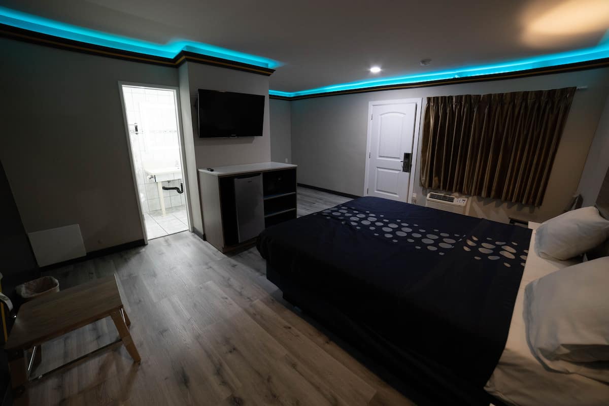 A modern hotel room with a bed, a TV, a desk, and a door leading to a balcony.