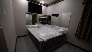 Un bagno moderno con una grande vasca, un mobile lavabo con specchio e un televisore a schermo piatto montato sopra lo specchio.