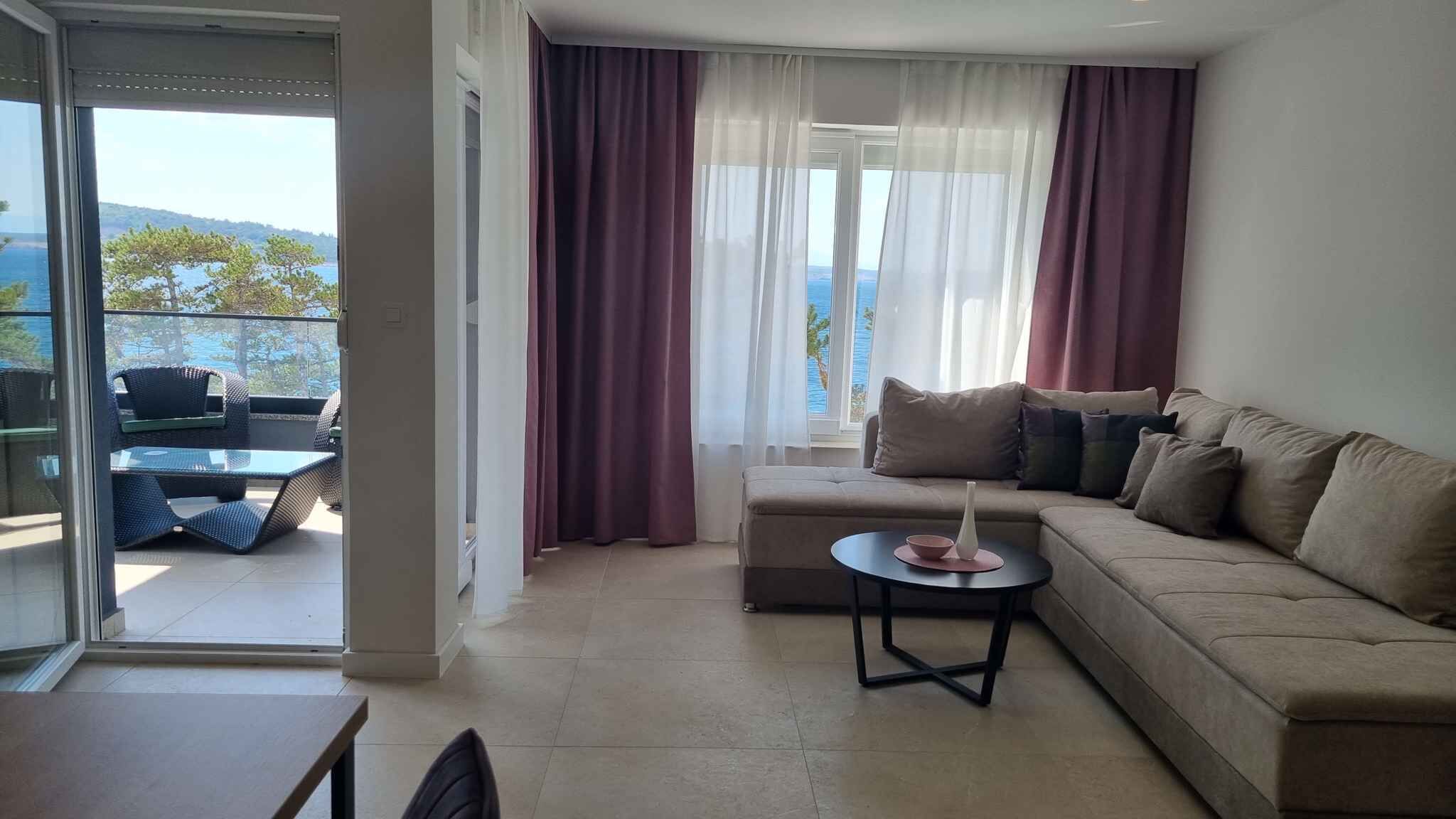 Un salon moderne avec un canapé, une petite table et une vue sur l’extérieur grâce à de grandes fenêtres.