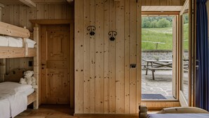 A wooden room with bunk beds, a door, and a view of an outdoor area with a picnic table.