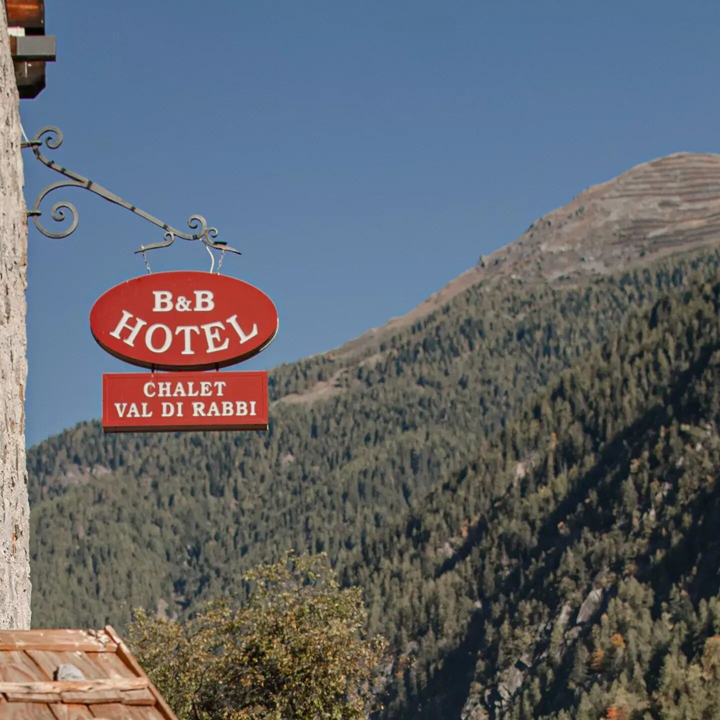 Señal de hotel con la inscripción "B&B HOTEL" y "CHALET VAL DI RABBI", que indica un bed and breakfast en una zona montañosa.