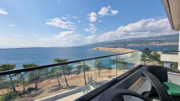 Un balcon avec vue sur la mer, une côte rocheuse et des bâtiments situés au loin.