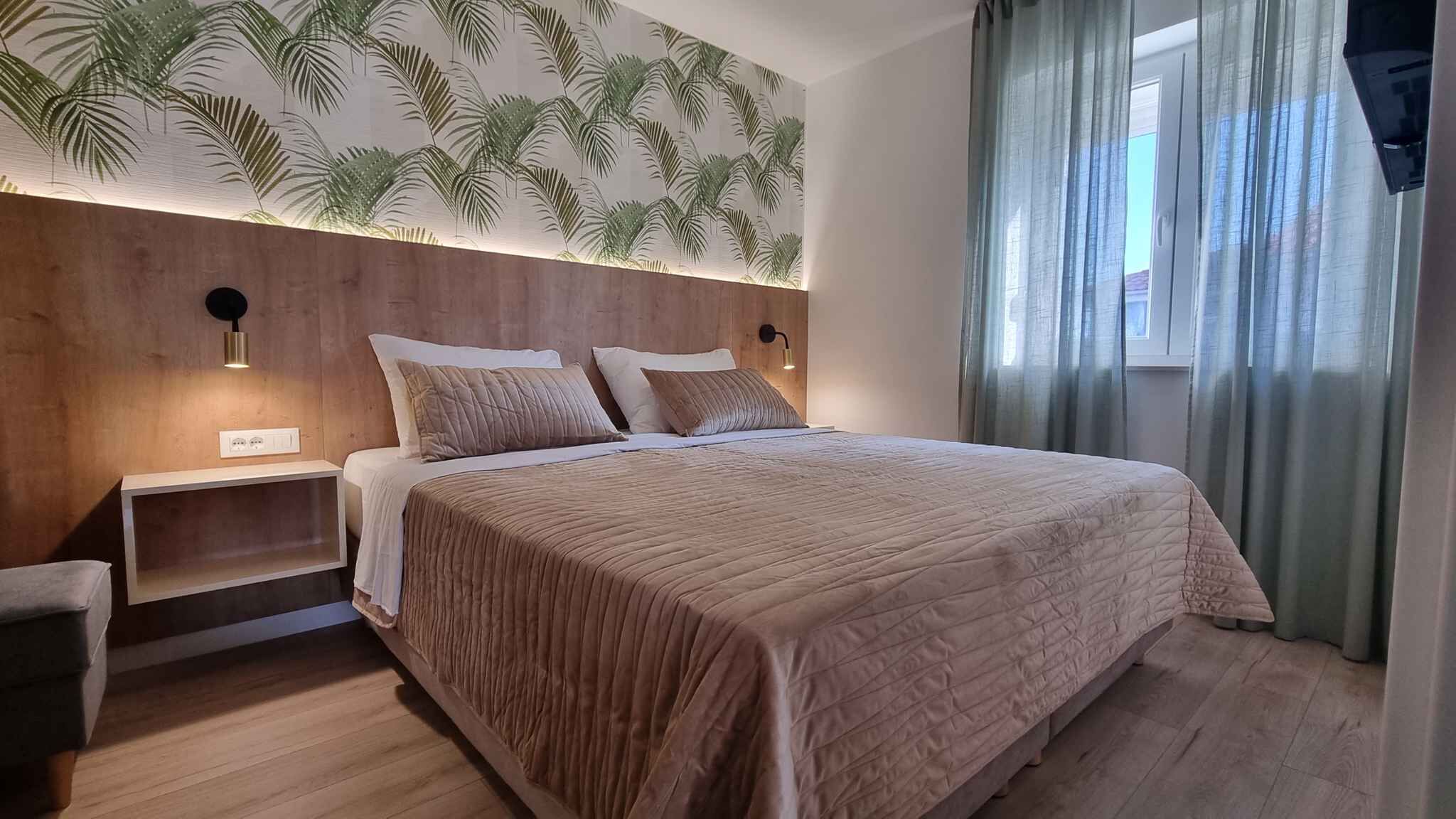 A bedroom with a large bed, wooden headboard, two bedside tables, a nightstand, and a wall with a leaf pattern.