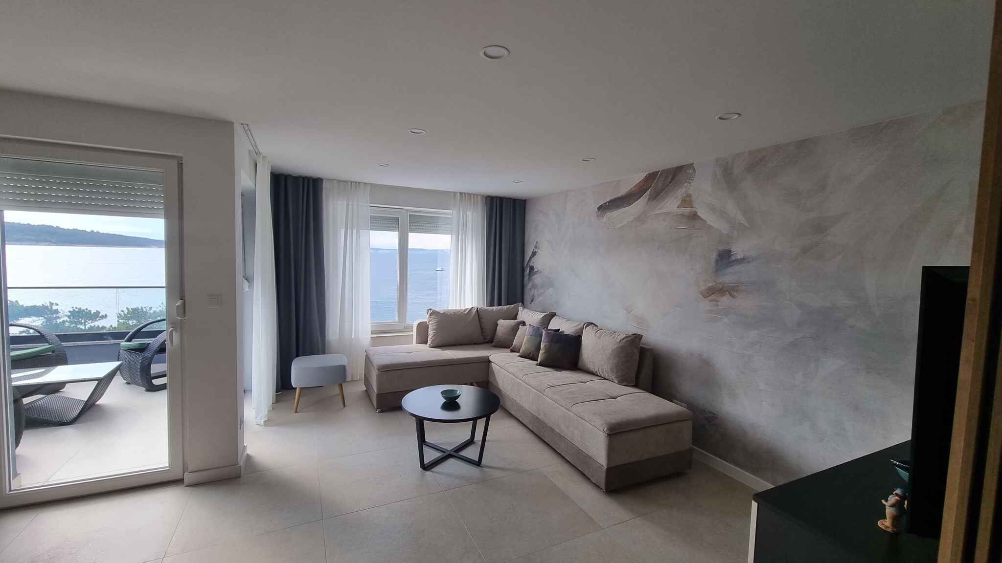 Un salon moderne avec un canapé, une petite table ronde et une vue sur la mer, visible à travers une porte-fenêtre coulissante.