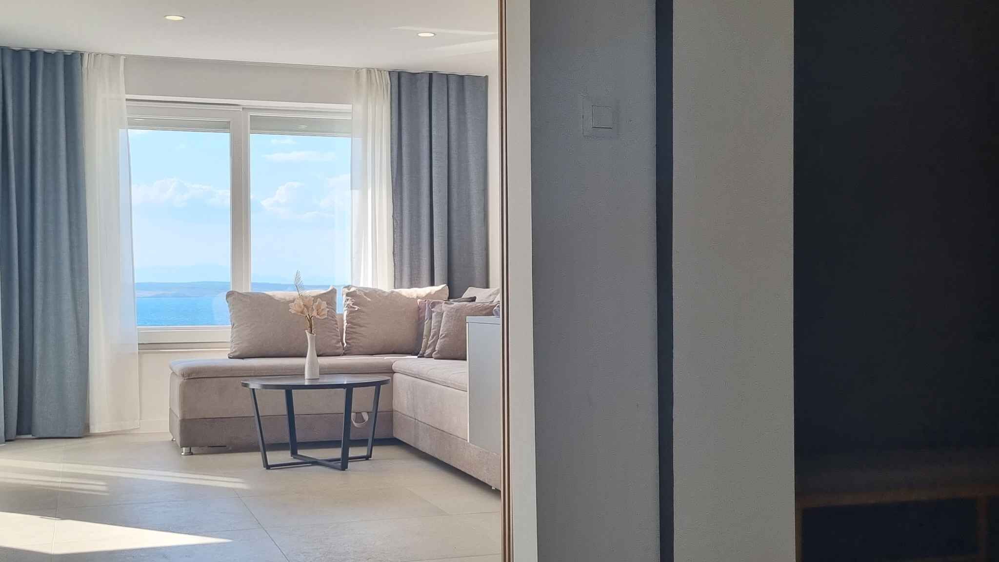 A modern living room with a sofa, a small table, and a view of the sea through large windows.