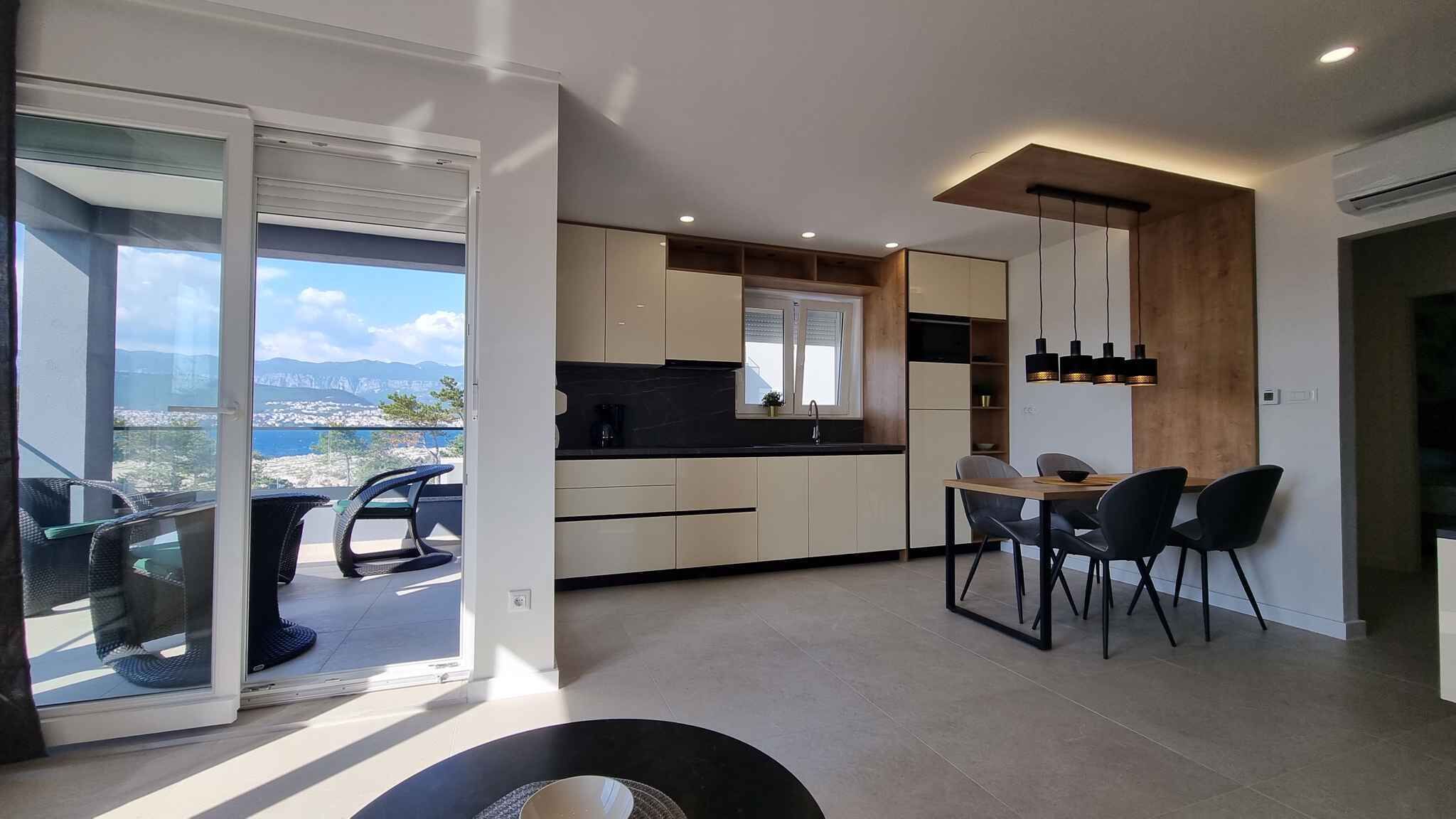 Moderni keittiö, jossa on ruokailutila ja suuret liukulasiovet, jotka johtavat parvekkeelle, jolta avautuu upea näkymä.