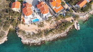 Oversigtsbillede af en ejendom ved kysten med flere bygninger, en swimmingpool og en bådehavn.