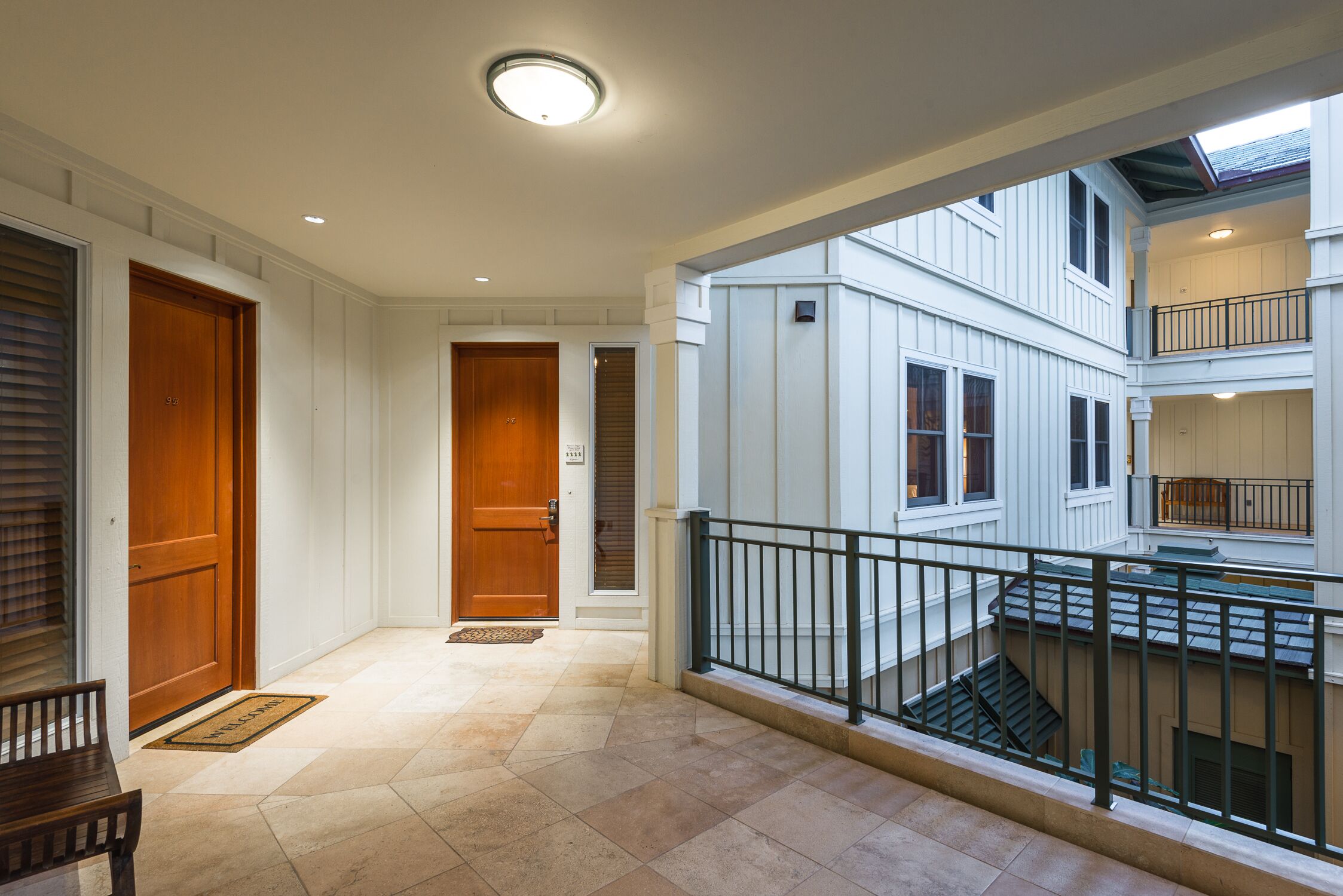 A spacious indoor area with a wooden bench, a staircase, and a view of a multi-level building.