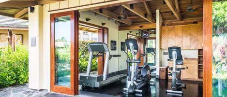 A covered outdoor gym area with exercise equipment, stone flooring, and wooden beams.