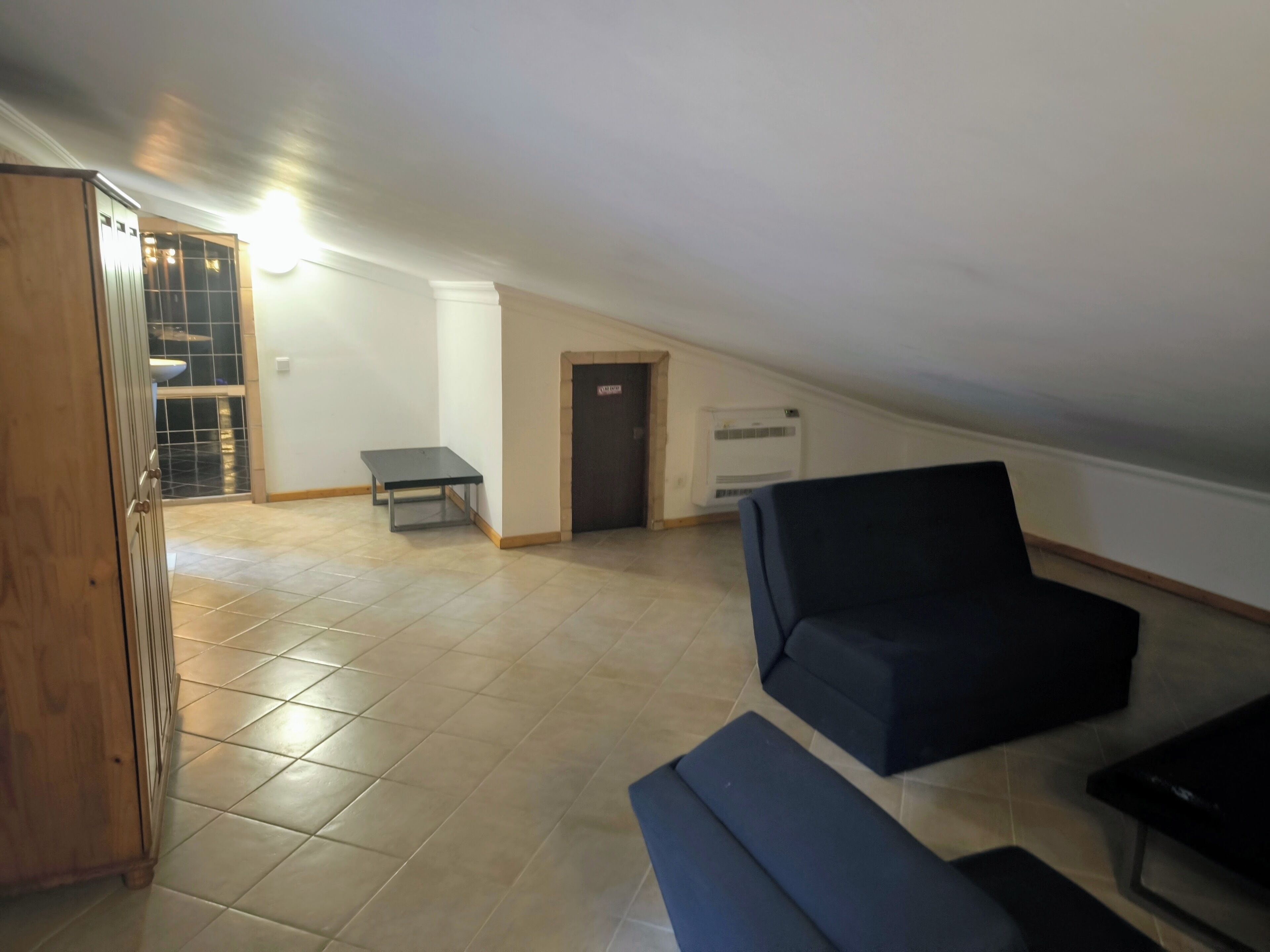 A spacious living area with a high ceiling, a dark-colored sofa, a small table, and a wooden cabinet.
