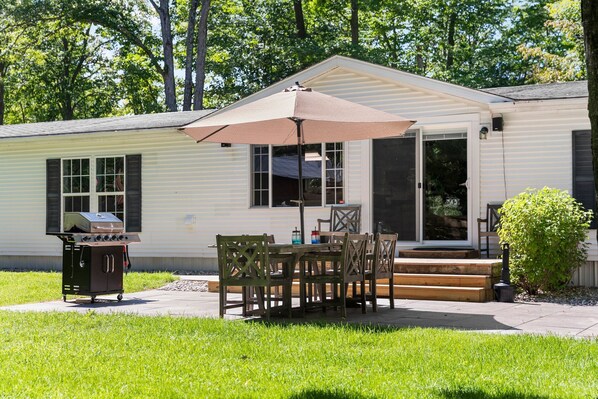 A small house with a patio, a grill, and a table with chairs.