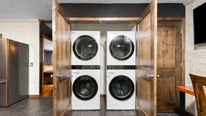 A laundry room with two front-loading washing machines, a wooden door, and a tiled floor.
