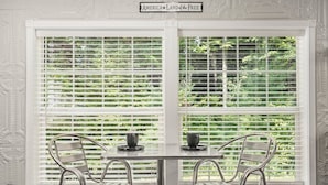 A dining area with a table and two chairs, a window with white blinds, and a sign above the window that reads "AMERICA LAND of the FREE".