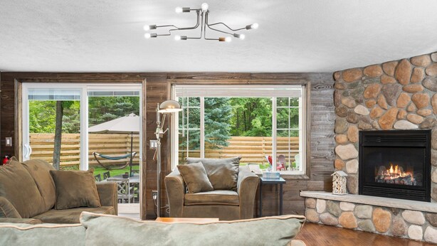 A cozy living room with a stone fireplace, a leather sofa, and a view of the outdoors through large windows.