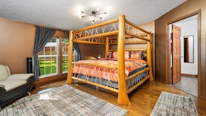 A four-poster bed with a wooden frame, a patterned bedspread, and a view of a garden through a large window.