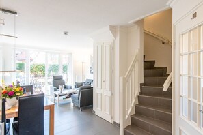 A spacious living area with a dining table, chairs, and a sofa. There is a staircase leading to an upper floor. - Haus Maybachstraße - Großzügig. Garten. Zentral. - ID: Mbs/22 (Sylt)