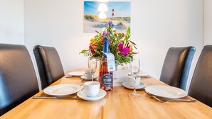 Ein Esstisch für vier Personen, dekoriert mit einem Blumenarrangement, einer Champagnerflasche und einem Gemälde eines Leuchtturms an der Wand.