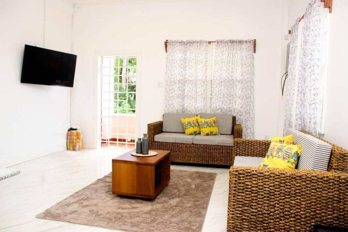 Un salón con un sofá de mimbre, una mesa de centro de madera y un televisor montado en la pared.