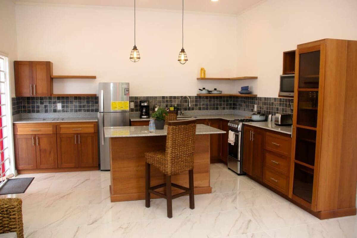 Una cocina moderna con una isla central, armarios de madera, horno integrado e iluminación colgante.