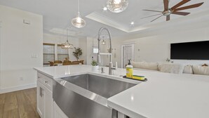 Una cocina moderna con un lavamanos grande de acero inoxidable, encimeras blancas y un ventilador de techo.