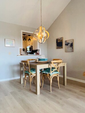 Un coin repas avec une table et des chaises en bois, un luminaire suspendu et une cuisine en arrière-plan.