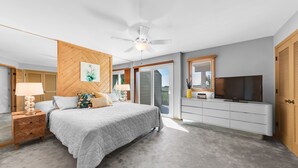 Une chambre à coucher comprenant un lit, une table de chevet, une lampe, un téléviseur et un ventilateur de plafond.