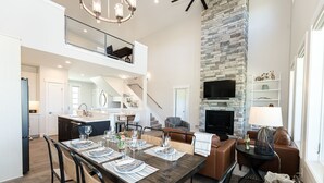 A spacious living area with a dining table set for six, a fireplace, and a stone accent wall. - Luxury Mountain Retreat - Hot Tub + Views!  (Granby)