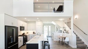 A modern kitchen with a central island, a dining area, and a staircase leading to an upper level. - Luxury Mountain Retreat - Hot Tub + Views!  (Granby)