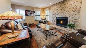 A living room with leather sofas, a wooden coffee table, a stone fireplace, and a television mounted on the wall.