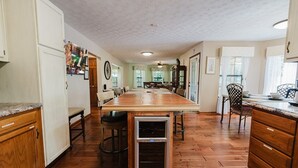 A spacious kitchen with a long wooden table, wooden cabinets, and a built-in wine cooler.