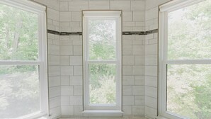 A corner room with three large windows, white tiled walls, and a bench at the base.