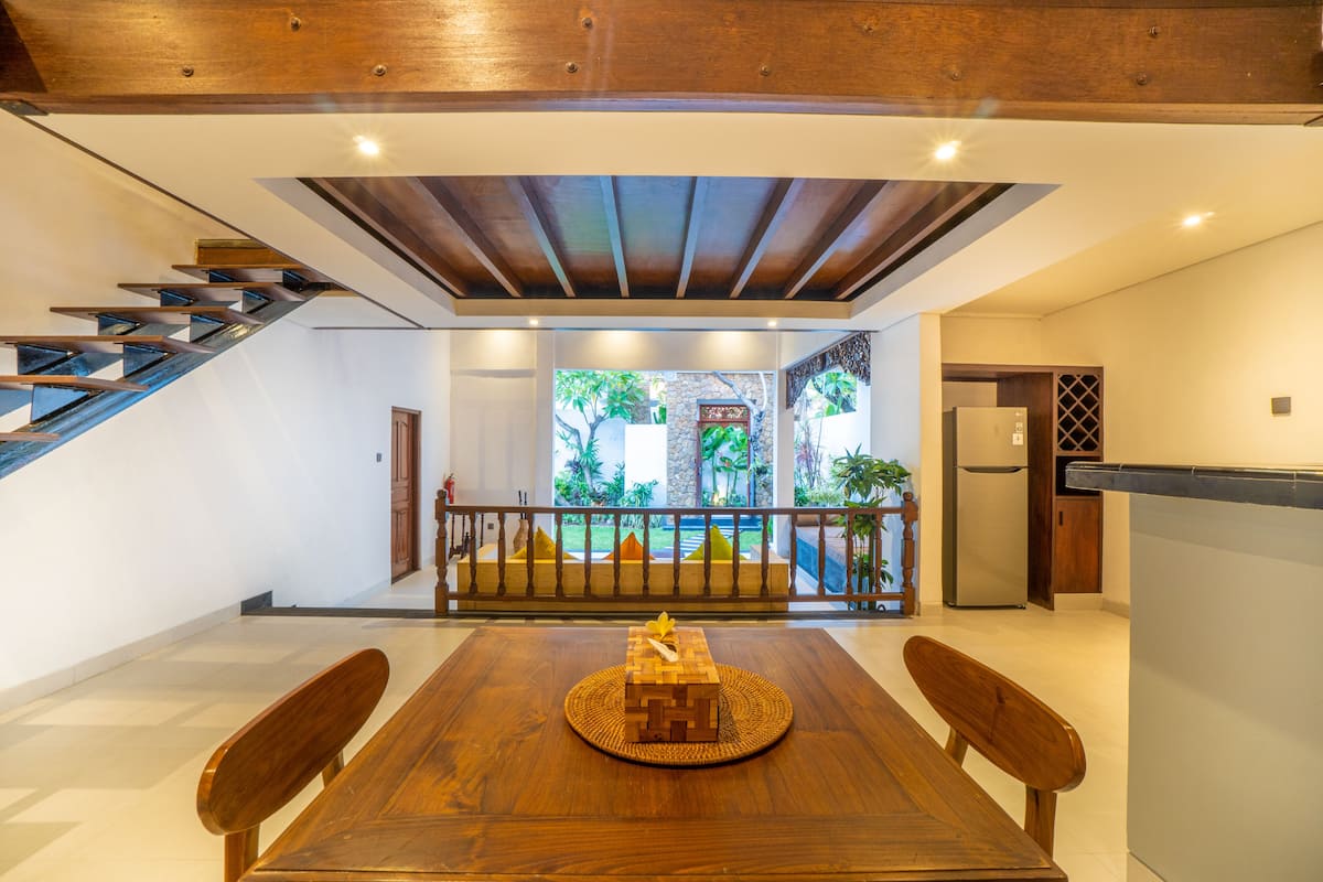 A modern kitchen with a built-in refrigerator, a wooden dining table with a placemat, and a staircase leading to an outdoor area with a view of greenery.