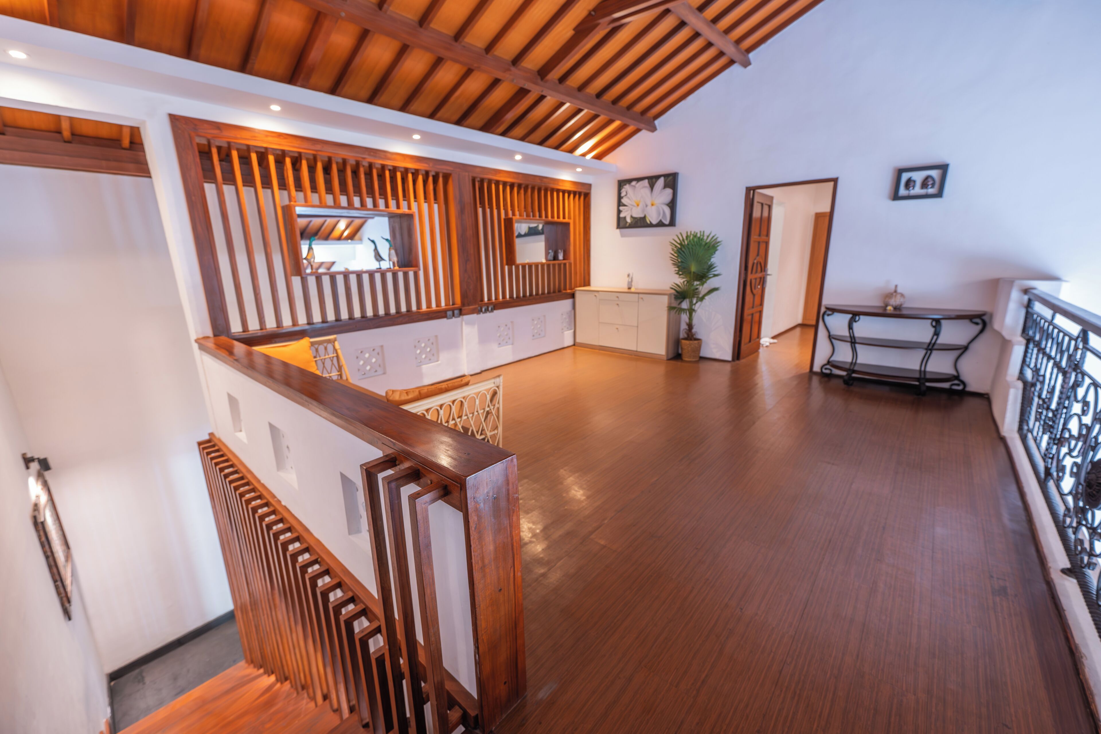 A spacious room with wooden flooring, a wooden staircase, a dining area with a table and chairs, and a potted plant.