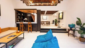 A modern living room with a sofa, a coffee table, and a blue bean bag. There is a kitchen area with a dining table and chairs. - Alam Jepun Villa  (Legian)