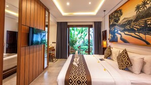 A modern hotel room with a large bed, a TV, a desk, and a view of greenery through the window. - Alam Jepun Villa  (Legian)
