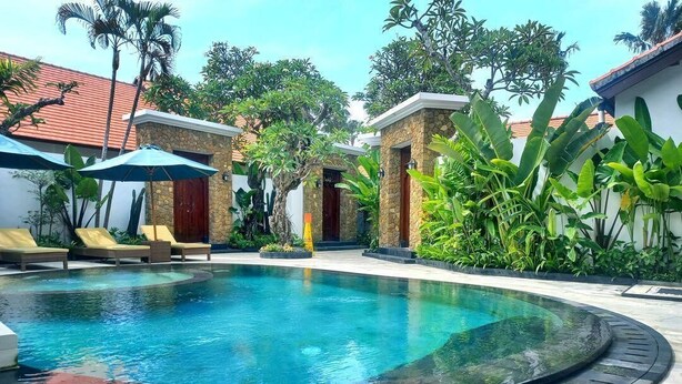 A circular pool with lounge chairs and umbrellas, surrounded by tropical plants and a stone building. - Alam Jepun Villa  (Legian)