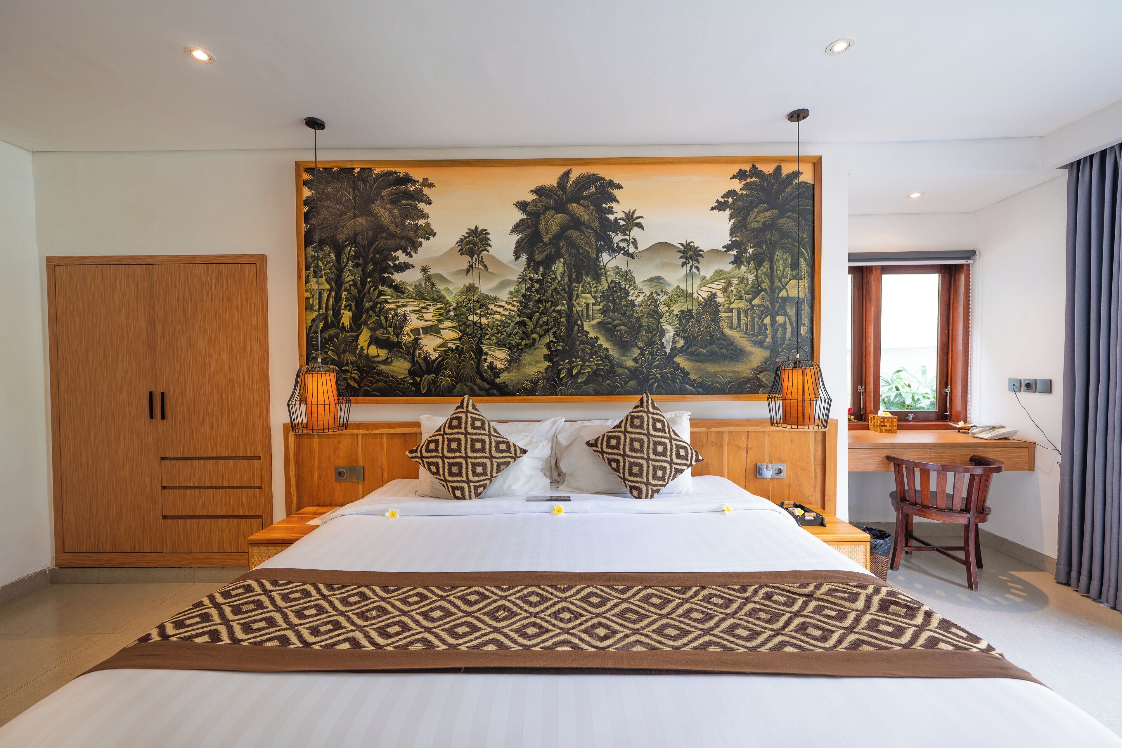 Une chambre à coucher avec un grand lit, une armoire en bois, un bureau et un grand tableau représentant un paysage tropical.