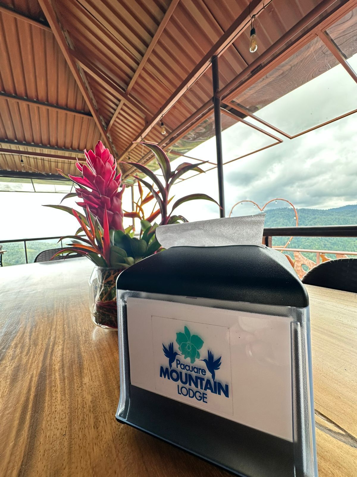 Una mesa con un letrero que indica Pacaure Mountain Lodge, techo de madera y vistas a las montañas.