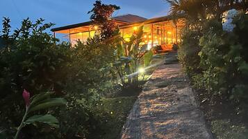 A pathway leading to a building with a glass facade, surrounded by lush greenery.