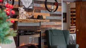 A cozy living room with a fireplace, a green armchair, and a wooden wall with a 'cher' sign. - The Bigfork Riverside Retreat - No Cleaning Fee! (Bigfork)