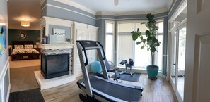 A home gym with exercise equipment, a fireplace, and a large window with blinds.