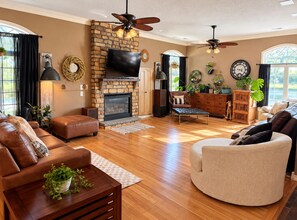 A spacious living room with a fireplace, leather sofas, a round coffee table, and a ceiling fan.