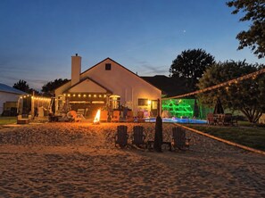 A building with a covered outdoor seating area, a pool, and a sandy foreground.
