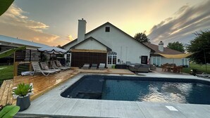 Un patio trasero con piscina, sillas de descanso y un área de patio techada.